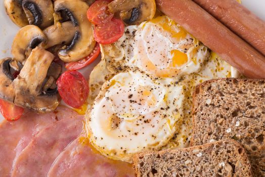 English breakfast with two fried eggs, two viennas, two slices of toast, three slices of fried ham and some fried mushrooms and baby tomatos.