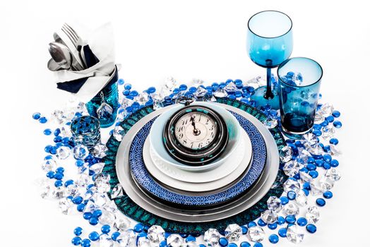 Table setting in the theme of new years eve with blue, and white. the centre piece of the setting is a large watch or clock set on one minute before midnight.