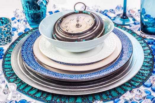 Table setting in the theme of new year, with blue, silver, and white. A clock as decoration points at one minute before midnight.