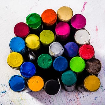 Multi couloured oil pastels standing up right in agroup or bundle and situated on white art paper that has been marked all over by the  coloured oil pastels.