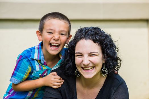 Portrait of a monther and her son outside on the lawn on a nice summer day, both looking at the camera and laughing happily. Son slightly behind mother with his hand on her sholder.