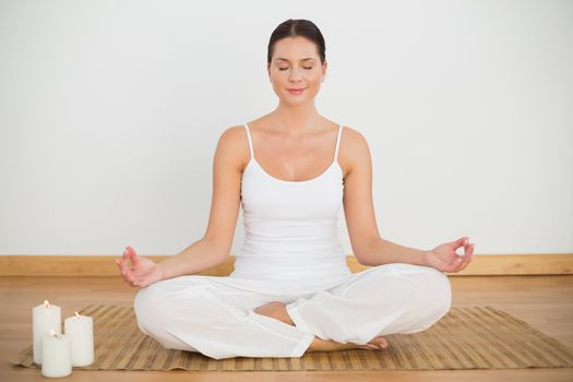 Smiling brunette sitting in lotus pose looking at camera in a white room