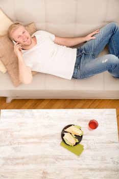 Young man with a Sandwich on the Sofa while talking on the phone.
