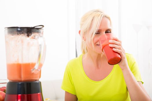 A beautiful mature woman enjoying a smoothie or juice with fruits in the kitchen.
