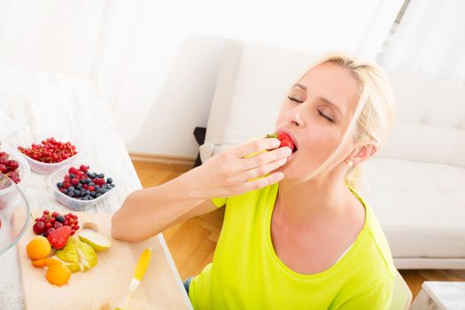 A beautiful mature woman eating strawberry at home.
