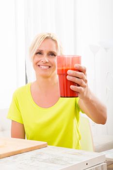 A beautiful mature woman enjoying a smoothie or juice with fruits in the kitchen.
