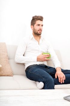 A young adult man sitting on couch with coffee.
