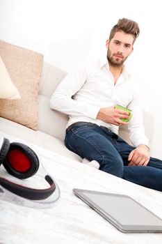 A young adult man sitting on the couch holding coffee.
