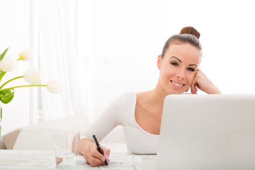 A young adult woman drawing an architectural plan at home with laptop and flowers.
