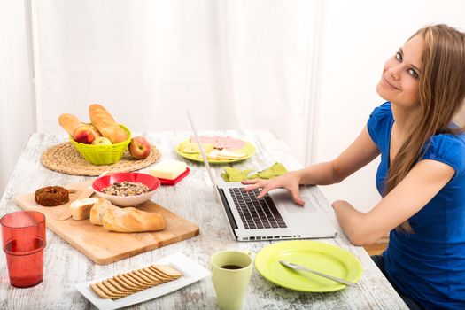 A young woman having breakfast while using a laptop computer.
