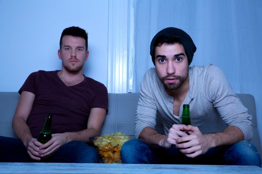 Two Friends watching passionately TV with Beer and Potato Chips.
