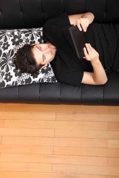 A young hispanic man lying on the sofa holding a Tablet PC.