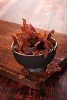 Beef jerky. Dried meat beef jerky on wooden chopping board on wooden background. Dry meat, rustic country style. Delicious meat eating. 