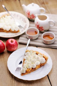 Apple tart with whipped cream, red apples and teaware on wood table