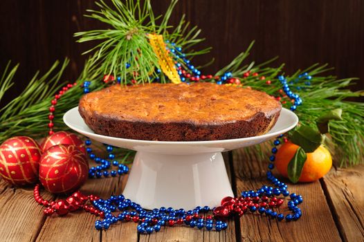 Christmas cake on white plate with fur tree, tangerine and christmas toys on wood table