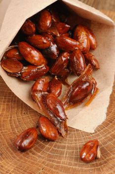 Almond in caramel in paper pack on wood plate