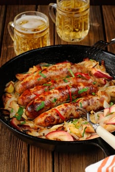 Sausages fried in cast iron skillet with two beer mugs on wooden background