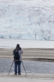 Active senior man wearing backpack and using a tripod photographs Mendenhall Glacier in Juneau, Alaska, in vertical image with copy space.