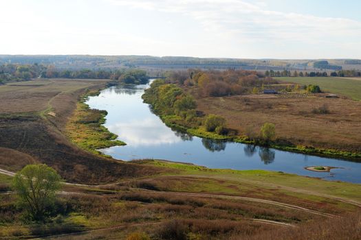 Autumn fields and narrow Zusha river with reflections of clouds