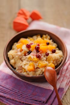 Millet porrige with pumpkin in clay bowl with wooden spoon on wooden background