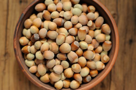Hazel nuts in clay bowl on wooden background