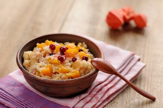 Millet porrige with pumpkin in clay bowl with wooden spoon on wooden background