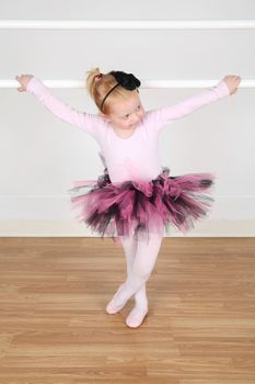 Little ballet girl standing at the barre in studio