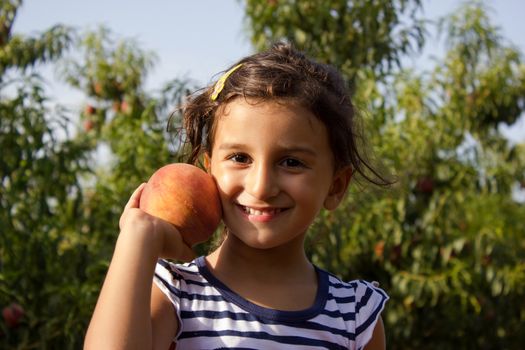 Cheerful little boy playing in the garden holding a peach