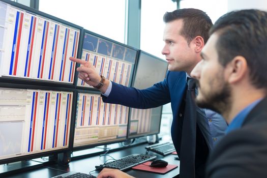 Businessmen trading stocks. Stock traders looking at graphs, indexes and numbers on multiple computer screens. Colleagues in discussion in traders office. 