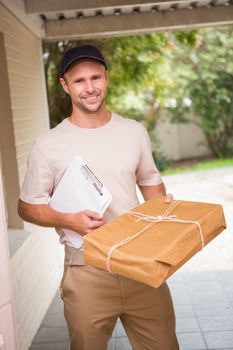 Delivery man smiling at camera offering parcel outside the warehouse