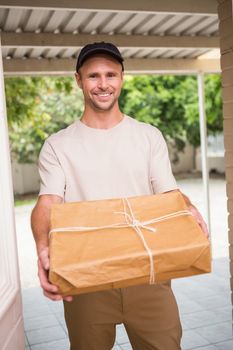 Delivery man smiling at camera offering parcel outside the warehouse