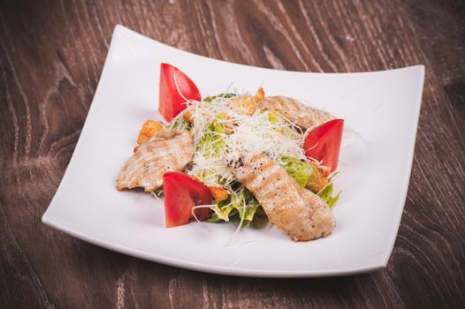 cesar salad with chiken, tomato, croutons and cheese on white plate 