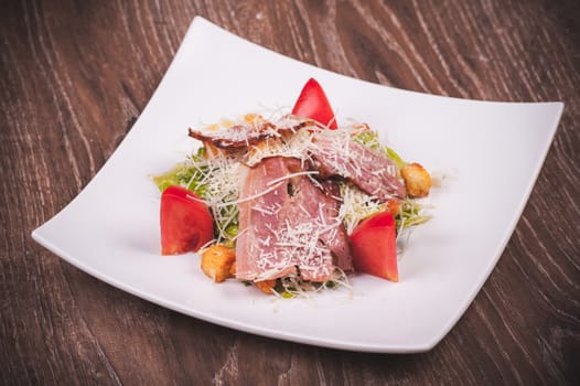 cesar salad with bacon, tomato, croutons and cheese on white plate 