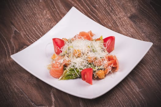 cesar salad with salmon, tomato, croutons and cheese on white plate