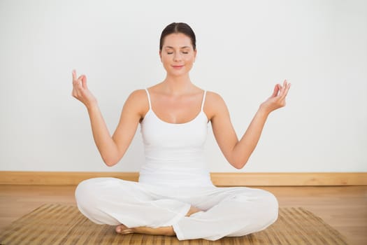 Smiling brunette sitting in lotus pose looking at camera in a white room