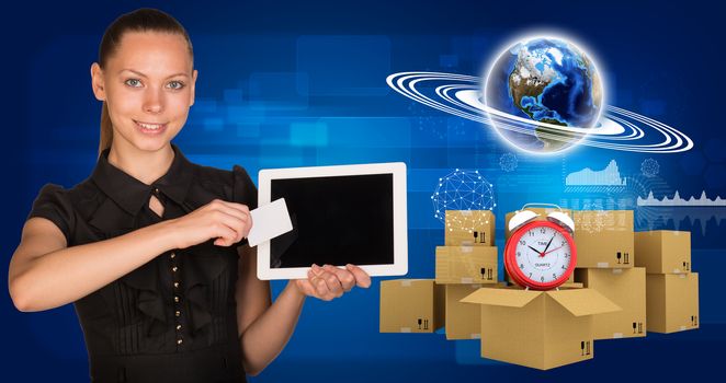 Beautiful businesswoman holding blank tablet PC and blank business card in front of PC screen.Beside are commodity boxes and alarm-clock on top of one of them. Globe surrounded by rings, graphs and other virtual elements as backdrop. Elements of this image furnished by NASA