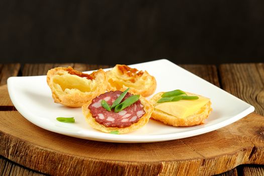 Gougeres with cheese and sausage on white plate and wood table