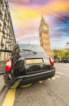 Black London cab under Big Ben tower and Westminster Palace.