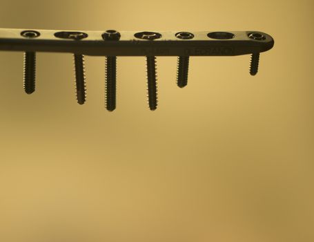 Traumatology orthopedic surgery implant plate and screws in semi silhouette against plain studio background. Closeup macro rectangular photograph. 