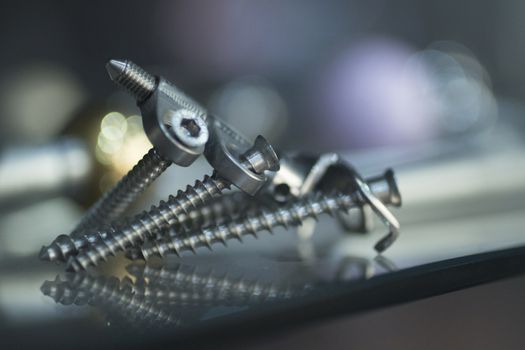 Traumatology orthopedic surgery implant plate and screws with artistic reflection and defocused background. Closeup macro vertical photograph in blue tones. 