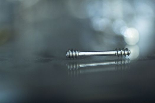 Closeup macro photo of traumatology orthopedic surgery implant metal double thread screw set against blue out of focus background. 