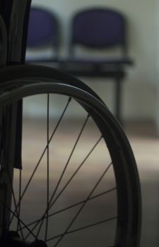 Wheel chair in hospital clinic artistic silhouette with waiting room chairs defocused behind. Color digital photo in warm tones shot from behind with shallow depth of focus