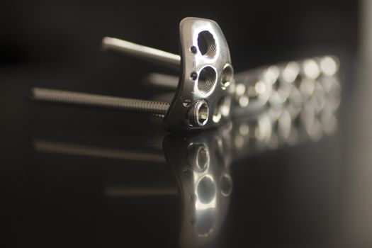 Traumatology orthopedic surgery implant titanium plate and silver color screws in semi silhouette against plain black studio background. Close-up macro photograph in grey tones with reflection and copy space. 