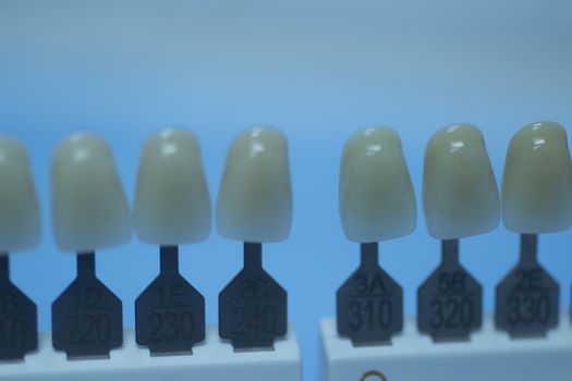 Dentist's tooth color guide used to choose the appropriate natural colors for a patient's tooth implants and crowns on plain blue background of the dental surgery clinic table. Close-up macro photo. 