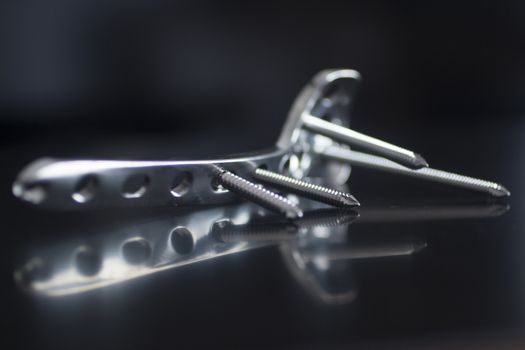 Traumatology orthopedic surgery implant titanium plate and silver color screws in semi silhouette against plain black studio background. Close-up macro photograph in grey tones with reflection and copy space. 
