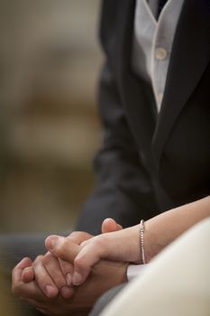 Color artistic digital photo of bridegroom in dark suit and white shirt with cufflinks in church religious wedding marriage ceremony holding hands with the bride in white wedding bridal dress. Shallow depth of with background out of focus. 