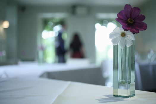 Color artistic digital rectangular horizontal photo of vase with red and white flowers on table in empty reception banquet marriage party room in Barcelona Spain. Shallow depth of with background out of focus.