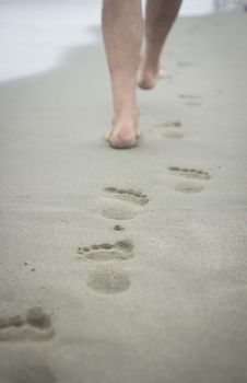 Vertical photo of feet of man and footprints on sand of beach on grey cold day with sea defocused in background. Taken in Viareggio in Tuscany Italy on the Mediteranean sea coast. 