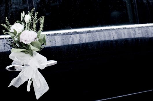 Color artistic digital rectangular horizontal photo of wedding bridal lace bow tied around white roses and flowers to limousine marriage car chrome door handle in Madrid Spain. 