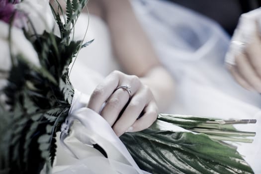 Color artistic digital rectangular horizontal photo of the bride's abridal bouquet of flowers with white silk bow held by bride before marriage ceremony in Spain. Shallow depth of with background out of focus of white wedding dress. 